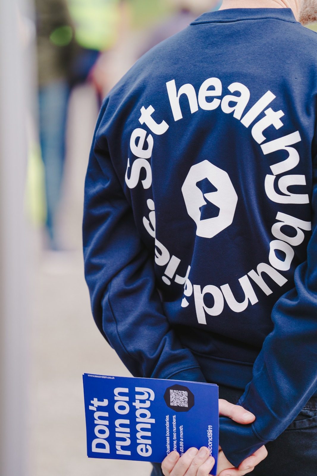 Back of a SecondSim sweatshirt reading Set healthy boundaries, holding a Don't run on empty flyer